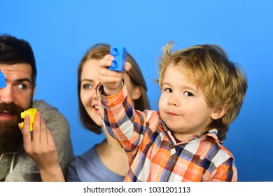 Family with curious faces spend time in playroom. Parents watch kid playing with yellow and blue bricks. Childhood and playing concept. Man with beard, woman and boy play on blue background. - Shutterstock ID 1031201113