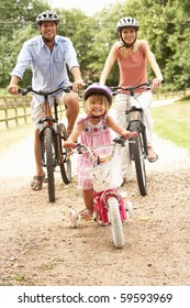 Family Cycling In Countryside Wearing Safety Helmets