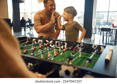 Family of dad, mother and son that are playing table football game indoors. - Powered by Shutterstock