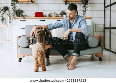 family dad young man soothe his son teenage cute boy on couch in cosy apartment with pet poodle dog, quality time with your family, upset teenager Foto stock © 