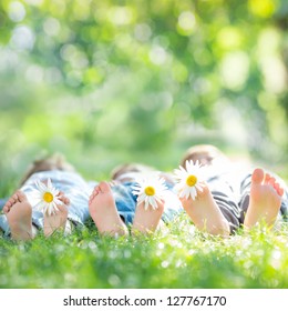 Family With Daisy Flowers Lying On Green Grass Against Spring Blurred Background