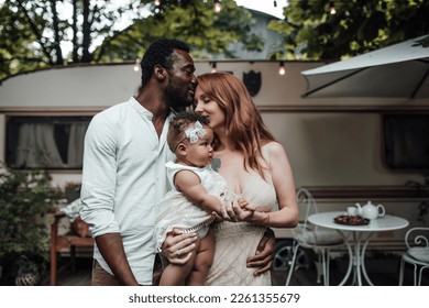Family with dark skinned infant daughter spend time together hugs and kisses in camper park. African american man his fair skin wife and little girl enjoying summer vacation in open air - Shutterstock ID 2261355679