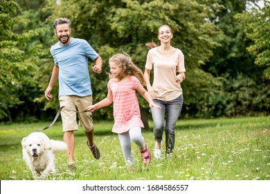 Family With Daughter And Dog Play Together In The Garden In Summer