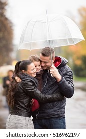 Family With Daughter Under The Umbrellas Walk On Rainy Day.