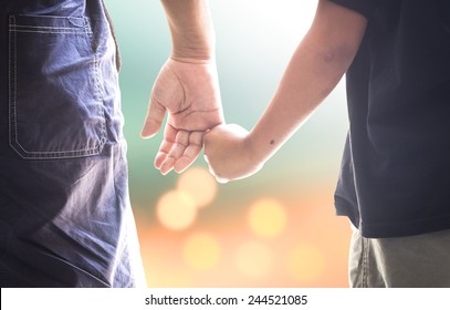 Family Day Concept: Autism Child Hand Holding Parent Finger On Blurred Autumn Sunset Background
