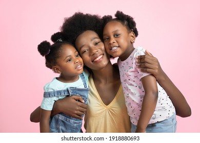 Family Day Concept. Close Up Studio Portrait Of Happy Young Dark Skinned Mommy With Her Cute Little Two Daughters, Smiling, Hugging And Having Fun Together, On Isolated Pink Background