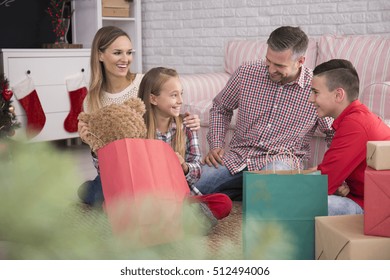 Family In Decorated Living Room Opening Bags With Christmas Gifts