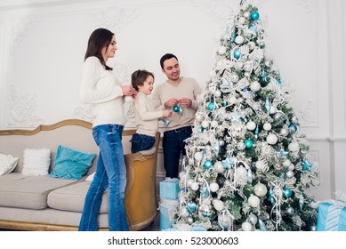 Family decorating a Christmas tree with boubles in the living-room