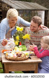 Family Decorating Easter Eggs On Table Outdoors