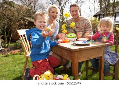 Family Decorating Easter Eggs On Table Outdoors