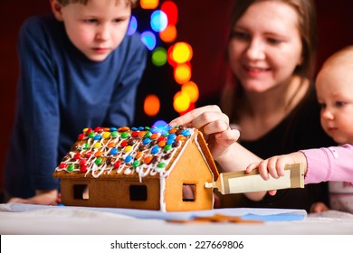 Family Decorating Gingerbread House On Christmas Eve. Focus On House