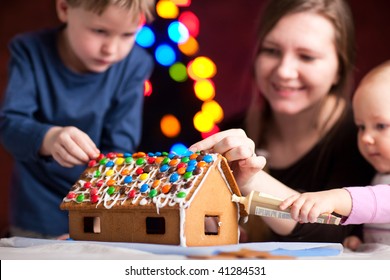 Family decorating gingerbread house on Christmas eve. Focus on house