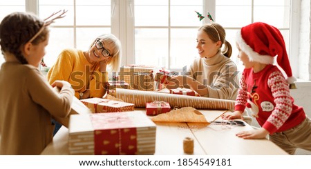 Family delighted kids gathering at table with mother and grandmother and wrapping presents in craft paper while smiling  
