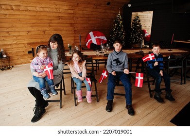 Family With Denmark Flags Inside Wooden House Sitting By Table. Travel To Scandinavian Countries. Happiest Danish People's .