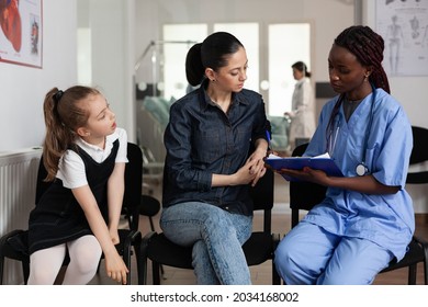 Family Discussing Medical Treatment With African American Nurse In Hospital Waiting Room During Clinical Appointment. African American Nurse Writing Clinical Expertise. Healthcare Support Service