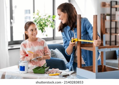 family, diy and home improvement concept - happy smiling mother and daughter with ruler measuring old wooden table for renovation at home