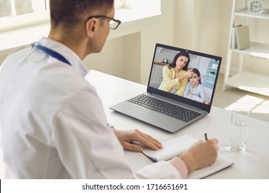 Family Doctor Online. Male Doctor Speaks With Patients By Family Using Laptop Sitting Behind Straw In Clinic Office.
