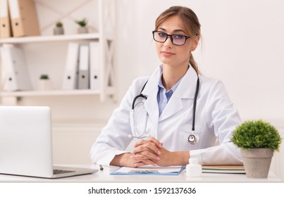 Family Doctor. Serious Lady Therapist Sitting At Laptop Looking At Camera In Modern Clinic Office. Selective Focus