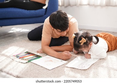 Family Does Homework At Home. Dad Helps Daughter On House's Floor. Mom Sits On Blue Couch On The Back. Kid Draws Picture On Paper.