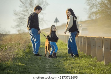 A Family With A Dog Makes A Hiking Trip With A Dog, Travelers With A Child Walk Along A Dusty Road