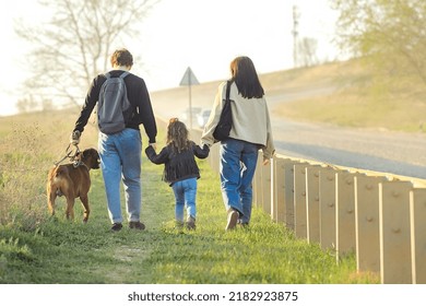 A Family With A Dog Makes A Hiking Trip With A Dog, Travelers With A Child Walk Along A Dusty Road