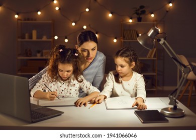 Family doing homework sitting at desk late in the evening. Focused mother and concentrated little kids working on school assignments together. Parent helping children to draw and write in copybooks