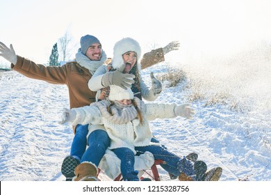 Family Doing Toboggan In Winter And Having Fun In The Snow