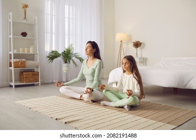 Family doing yoga for a good start of the day. Mom and kid enjoying yoga on quiet morning at home. Peaceful, tranquil mother together with calm child meditating in cross legged asana on bedroom floor