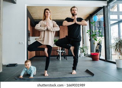 Family doing yoga. Mother and father standing in a position, keeping balance, while their child creeping on all fours at their feet.