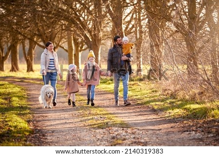 Family With Down Syndrome Daughter Walking With Pet Dog In Autumn Or Winter Countryside Together
