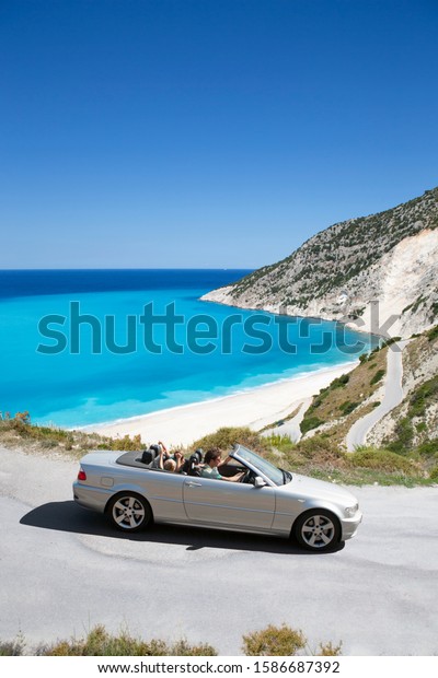 Family\
driving convertible car along winding coastal\
road