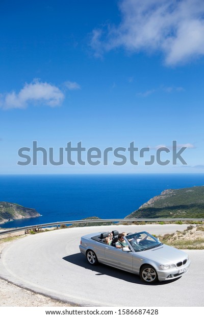 Family\
driving convertible car along winding coastal\
road