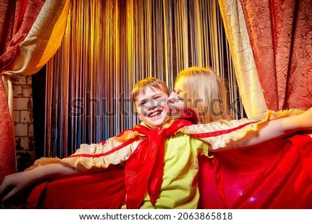 Family during a stylized theatrical circus photo shoot in a beautiful red location. Models mother and son posing on stage with curtain