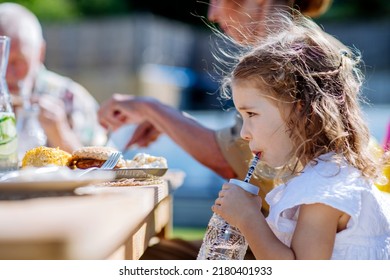 Family Eating At Barbecue Party Dinner In Garden, Little Girl Drinking Water And Enjoying It.