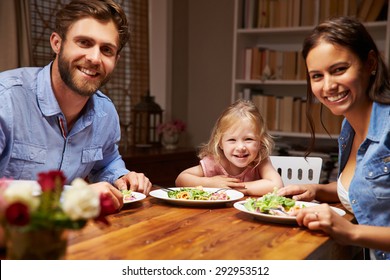 Family eating dinner at a dining table, looking at camera