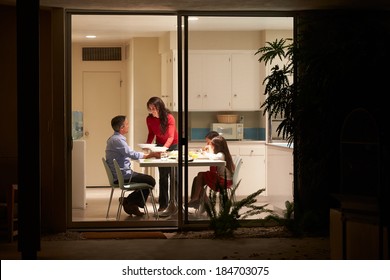 Family Eating Evening Meal Viewed From Outside