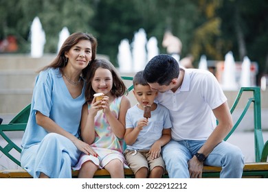 Family Eating Ice Cream On A Bench In The Summer Park. Selective Focus, Blurred Background. Happy Childhood. Parent Care.