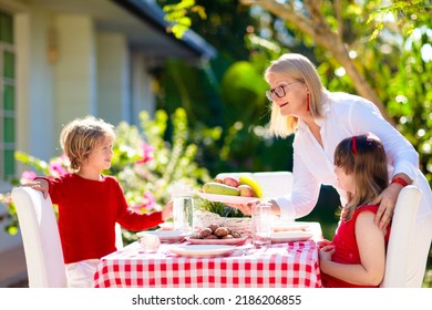 Family Eating Outdoors. Garden Summer Fun. Barbecue In Sunny Backyard. Grandmother And Kids Eat Lunch In Outdoor Deck. Parents And Children Enjoy Bbq. Boy And Girl With Mother.