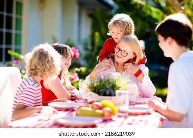 Family Eating Outdoors. Garden Summer Fun. Barbecue In Sunny Backyard. Grandmother And Kids Eat Lunch In Outdoor Deck. Parents And Children Enjoy Bbq. Boy And Girl With Mother.