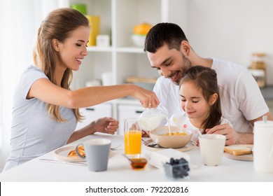 family, eating and people concept - happy mother, father and daughter having breakfast at home