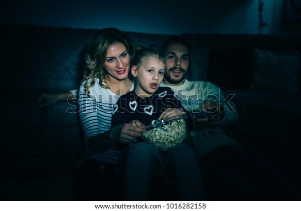 Family eating\
popcorn while watching tv at\
home