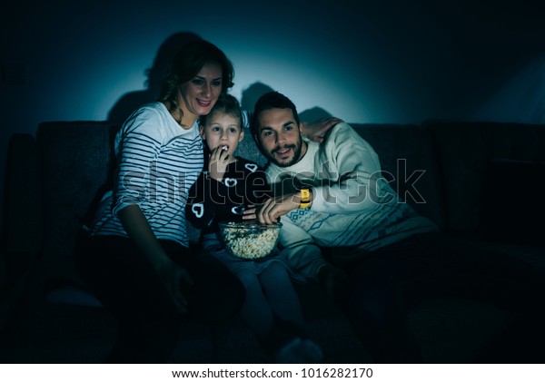 Family eating\
popcorn while watching tv at\
home