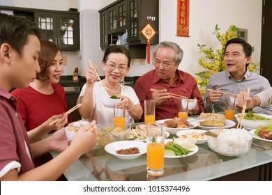 Family eating various traditional dishes at Tet celebration. Scrolls wishing luck and wealth in the background