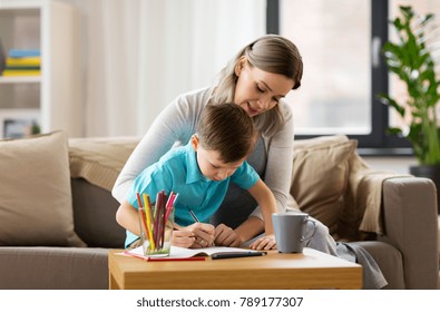family and education concept - happy mother and little son with workbook writing or drawing at home