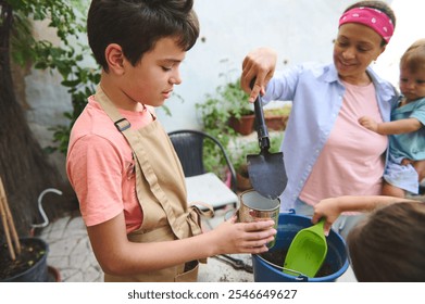 A family engages in a gardening activity outdoors. A young boy, with assistance, fills a recycled can with soil. The scene radiates family bonding, learning, and teamwork. - Powered by Shutterstock