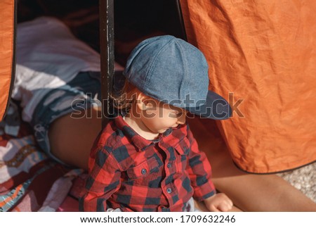 Family enjoying camping holiday in countryside. Little child sitting in front of the camping tent, while parents sleeping inside, show their feets