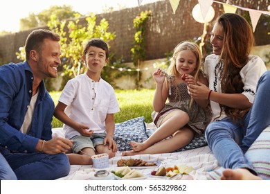 Family Enjoying Picnic On Blanket In Garden