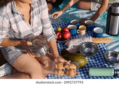 A family enjoying a picnic outdoors with various foods and drinks, including fresh fruit, pastries, and coffee. The setting is relaxed and happy. - Powered by Shutterstock