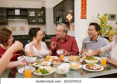 Family enjoying talk and good food at Chinese New Year celebration. Scrolls wishing luck and wealth in the background