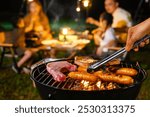 Family enjoys a cozy evening barbecue outdoors. The focus is on the grill, with sausages and meat cooking, while the family sits in the background, enjoying the warm, festive atmosphere.